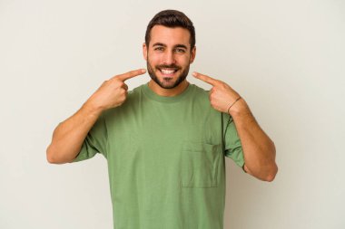 Beyaz arka planda izole edilmiş genç beyaz adam gülümsüyor, parmaklarını ağıza doğrultuyor..