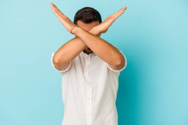 Kafkasyalı genç adam mavi arka planda izole edilmiş iki kolu çapraz tutuyor, inkar kavramı.