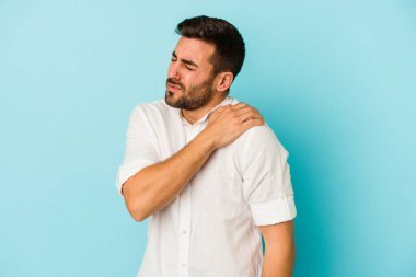 Mavi arka planda izole edilmiş, omuz ağrısı olan genç beyaz bir adam..