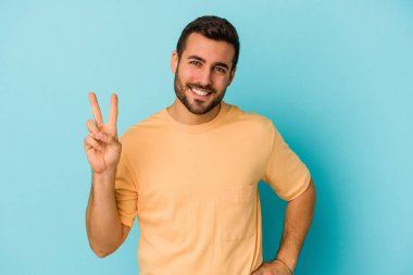 Mavi arka planda izole edilmiş genç beyaz adam iki numarayı parmaklarıyla gösteriyor..