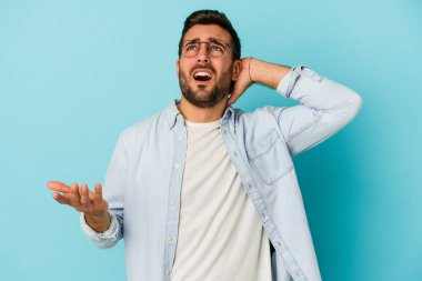 Mavi arka planda izole edilmiş genç beyaz adam öfkeyle bağırıyor..