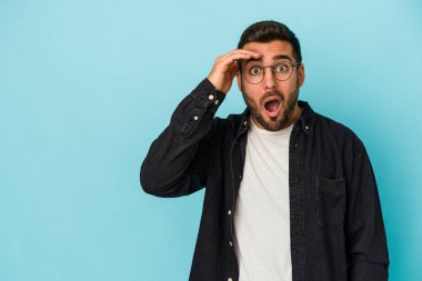 Kafkasyalı genç adam mavi arka planda izole edilmiş, uzaklara bakıyor ve elini alnına koyuyor..