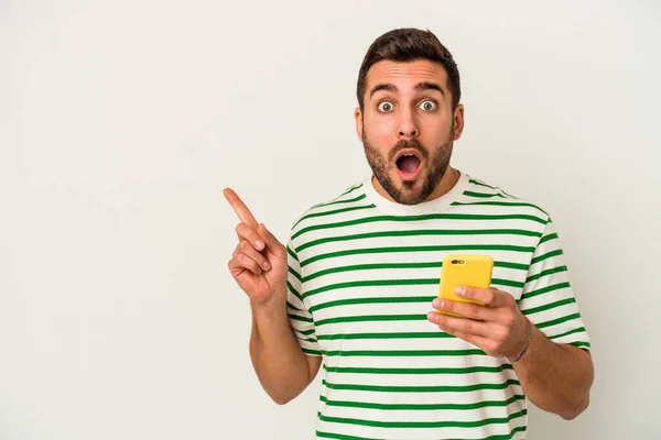 Jovem Caucasiano Segurando Telefone Celular Isolado Fundo Branco Apontando Para — Fotografia de Stock