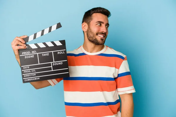 Young Caucasian Man Holding Clapperboard Isolated Blue Background Looks Aside — Stock Photo, Image