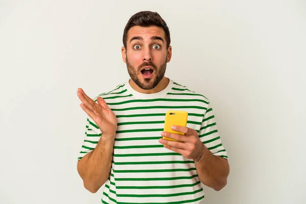 Jovem Caucasiano Segurando Telefone Celular Isolado Fundo Branco Surpreso Chocado — Fotografia de Stock