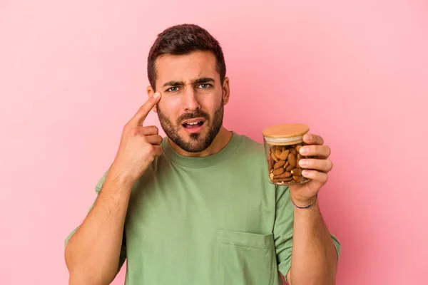 Joven Caucásico Sosteniendo Frasco Almendras Aislado Sobre Fondo Rosa Mostrando — Foto de Stock