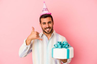 Pembe arka planda izole bir şekilde doğum gününü kutlayan genç beyaz adam parmaklarıyla bir cep telefonu hareketi gösteriyor..