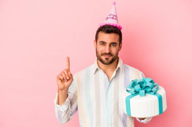 Pembe arka planda izole bir şekilde doğum gününü kutlayan beyaz bir adam bir numarayı parmağıyla gösteriyor..