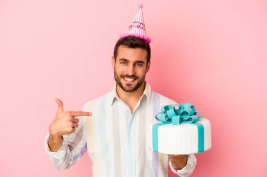 Doğumgününü kutlayan beyaz bir adam pembe arka planda yalnız başına gömlek fotokopi alanını gösteren gururlu ve kendinden emin birini işaret ediyor.