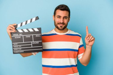 Kafkasyalı genç bir adam mavi arka planda bir numarayı parmağıyla gösteriyordu..