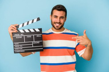 Mavi arka plandaki el kamerasından izole edilmiş, gururlu ve kendinden emin beyaz bir adam tişört fotokopi odasını işaret ediyor.