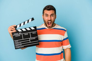 Kafkasyalı genç bir adam mavi arka planda izole edilmiş bir alçıpan tutuyor. Çok sinirli ve agresif bağırıyor..