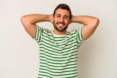 Beyaz arka planda izole olmuş genç beyaz bir adam kendini güvende hissediyor, elleri başının arkasında..