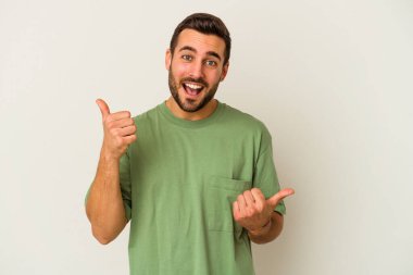 Beyaz arka planda izole edilmiş genç beyaz bir adam iki parmağını da kaldırıyor, gülümsüyor ve kendinden emin..