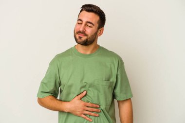 Beyaz arka planda izole edilmiş genç beyaz adam karnına dokunuyor, nazikçe gülümsüyor, yemek yiyor ve tatmin oluyor..