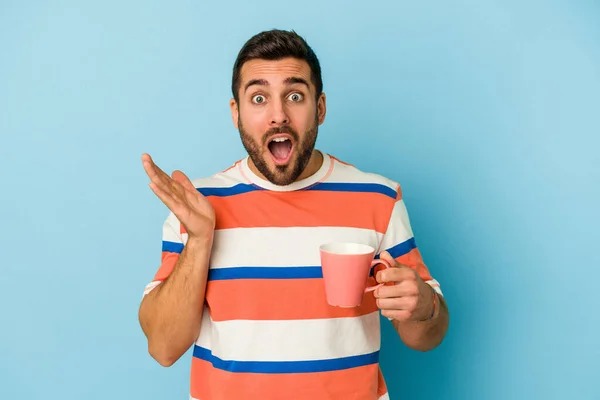 Young Caucasian Man Holding Mug Isolated Blue Background Surprised Shocked — Stock Photo, Image