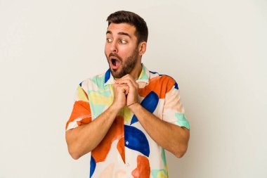 Beyaz arka planda izole edilmiş genç beyaz bir adam şans için dua ediyor, şaşırmış ve ağzını açıp önüne bakıyor..