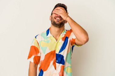 Beyaz arka planda soyutlanmış beyaz tenli genç bir adam elleriyle gözlerini kapatıyor, geniş bir gülümsemeyle bir sürpriz bekliyor..