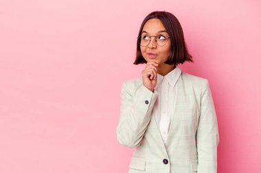 Pembe arka planda izole edilmiş yeşil takım elbiseli genç bir ırk kadını şüpheli ve şüpheci bir ifadeyle yana bakıyor..