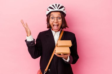 Pembe arka planda izole edilmiş bisiklet kaskı takan genç iş kadını hoş bir sürpriz bekliyor, heyecanlı ve el kaldırıyor..