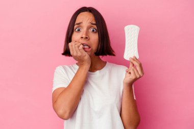 Elinde pembe arka planda, tırnak yiyen, gergin ve endişeli bir kompres tutan genç bir ırk kadını..