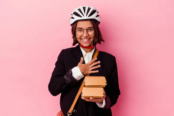 若いビジネス混合レースの女性を着て自転車ヘルメット保持ハンバーガーピンクの背景に隔離された笑いアウト大声で手を胸に保つ — ストック写真