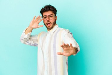 Mavi arka planda izole genç beyaz adam yakın bir tehlike nedeniyle şoka uğruyor