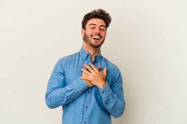 Beyaz arka planda soyutlanmış beyaz tenli genç bir adam gülüyor, elini yüreğine koyuyor, mutluluk kavramını koruyor..