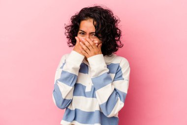 Genç kıvırcık Latin kadın pembe arka planda izole edilmiş ağzını kapayan elleri endişeli görünüyor..