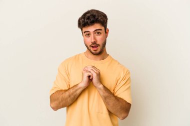 Beyaz arka planda izole edilmiş genç beyaz bir adam şans için dua ediyor, şaşırmış ve ağzını açıp önüne bakıyor..