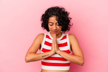 Genç kıvırcık Latin kadın pembe arka planda izole edilmiş dua ediyor, bağlılık gösteriyor, dindar biri ilahi ilham arıyor..