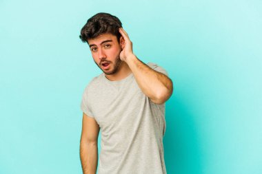 Mavi arka planda izole edilmiş genç beyaz adam bir dedikoduyu dinlemeye çalışıyor..