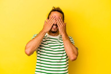 Sarı arka planda izole edilmiş uzun saçlı, genç beyaz bir adam. Gözleri ellerle kaplıyor. Gülümsüyor ve bir sürpriz bekliyor..