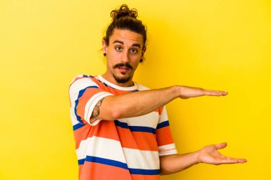 Sarı arka planda uzun saçlı beyaz bir adam iki eliyle bir şey tutuyor, ürün sunumu..