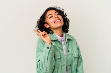 Beyaz arka planda izole edilmiş genç kıvırcık Latin kadın neşeli ve kaygısız parmaklarıyla barış sembolü gösteriyor..