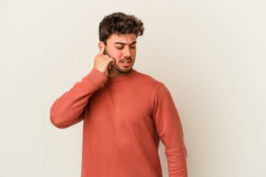 Beyaz arka planda izole edilmiş genç beyaz bir adam kulaklarını elleriyle kapatıyor..