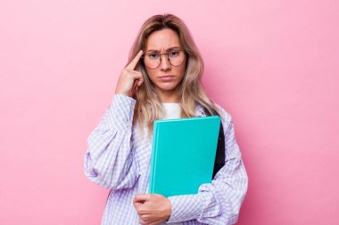 Genç Avustralyalı bir öğrenci pembe arka planda izole edilmiş. Parmağıyla tapınağı işaret ediyor, düşünüyor ve bir göreve odaklanıyor..