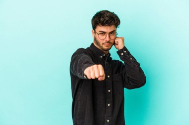Kafkasyalı genç bir adam mavi arka planda izole edilmiş. Yumruk atıyor, sinirleniyor, kavga ediyor, kavga ediyor..