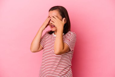 Pembe arka planda soyutlanmış orta yaşlı beyaz kadın elleriyle gözlerini kapatmaktan korkuyor..