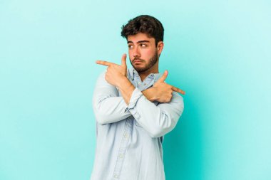 Mavi arka plan noktalarında izole genç beyaz adam, iki seçenek arasında seçim yapmaya çalışıyor.