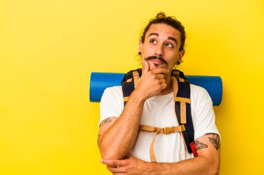 Sarı arka planda izole edilmiş uzun saçlı, beyaz tenli genç adam şüpheli ve şüpheci bir ifadeyle yana bakıyor..