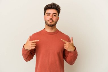 Beyaz arka planda yaşayan beyaz tenli genç bir adam gömlek fotokopi alanını gösteriyor, gururlu ve kendinden emin.