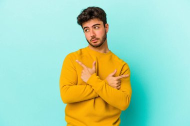 Mavi arka plan noktalarında izole genç beyaz adam, iki seçenek arasında seçim yapmaya çalışıyor.