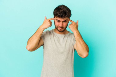 Kafkasyalı genç adam mavi arka planda izole edilmiş bir göreve odaklanmış, parmaklarını işaret ediyor..