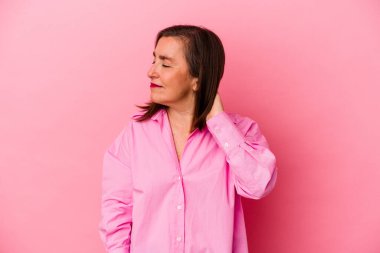 Pembe arka planda izole edilmiş orta yaşlı beyaz kadın stresten dolayı boynu ağrıyor, masaj yapıyor ve elle dokunuyor..