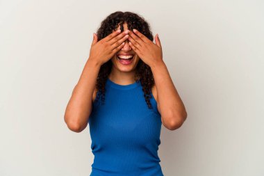 Beyaz arka planda soyutlanmış genç bir ırk kadını elleriyle gözlerini kapatıyor, gülümseyerek bir sürpriz bekliyor..