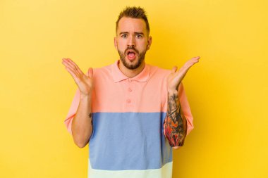 Sarı arka planda izole edilmiş genç dövmeli beyaz adam şaşırdı ve şok oldu..