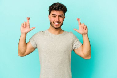 Kafkasyalı genç adam mavi arka planda izole edilmiş şans dilemek için şans diliyor.