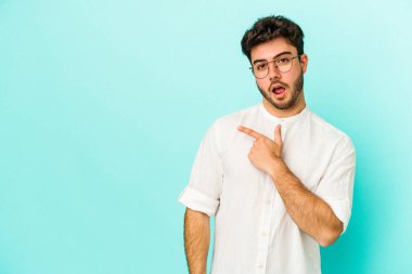 Mavi arka planda izole edilmiş genç beyaz adam yan tarafı işaret ediyor.