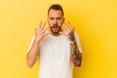 Sarı arka planda izole edilmiş genç dövmeli beyaz adam on numarayı elleriyle gösteriyor..